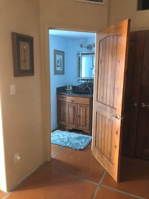 A hallway leading to a bathroom with a wooden door, a sink, and cabinets. - Pleasant 2-bedroom Casita in Tucson perfect for a relaxing getaway (Tucson)