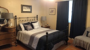 Un dormitorio con cama, mesitas de noche, lámpara, silla y ventana con cortinas.
