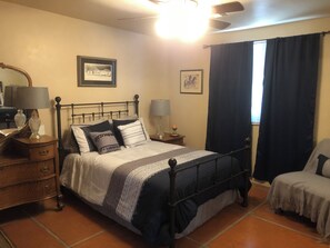 A bedroom with a bed, bedside tables, a lamp, a chair, and a window with curtains. - Pleasant 2-bedroom Casita in Tucson perfect for a relaxing getaway (Tucson)