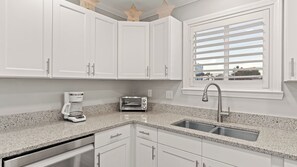 A modern kitchen with white cabinets, a built-in toaster, a coffee maker, and a stainless steel sink. - Seawinds 1 by Avantstay Beachfront + Private Beach + Daily Chair Service + 3 Decks (Miramar Beach)
