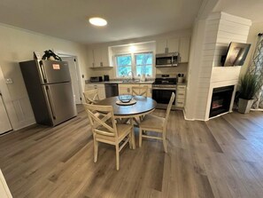 A kitchen with a dining table, chairs, a refrigerator, microwave, oven, and a fireplace. - Minutes to Beaches • Self Check-In • Fully Remodeled • Screened Porch • Cozy Fireplace • Washer & Dryer (Wilmington)