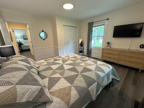A bedroom with a large bed, a dresser, a television, and a window with curtains. - Minutes to Beaches • Self Check-In • Fully Remodeled • Screened Porch • Cozy Fireplace • Washer & Dryer (Wilmington)