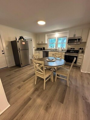 A compact kitchen with a central island, stainless steel appliances, and a window providing natural light. - Minutes to Beaches • Self Check-In • Fully Remodeled • Screened Porch • Cozy Fireplace • Washer & Dryer (Wilmington)