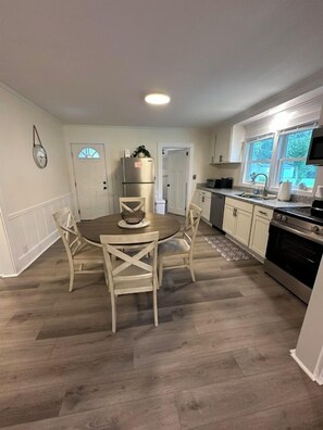 A kitchen with a round dining table, chairs, a refrigerator, and a stove. - Minutes to Beaches • Self Check-In • Fully Remodeled • Screened Porch • Cozy Fireplace • Washer & Dryer (Wilmington)
