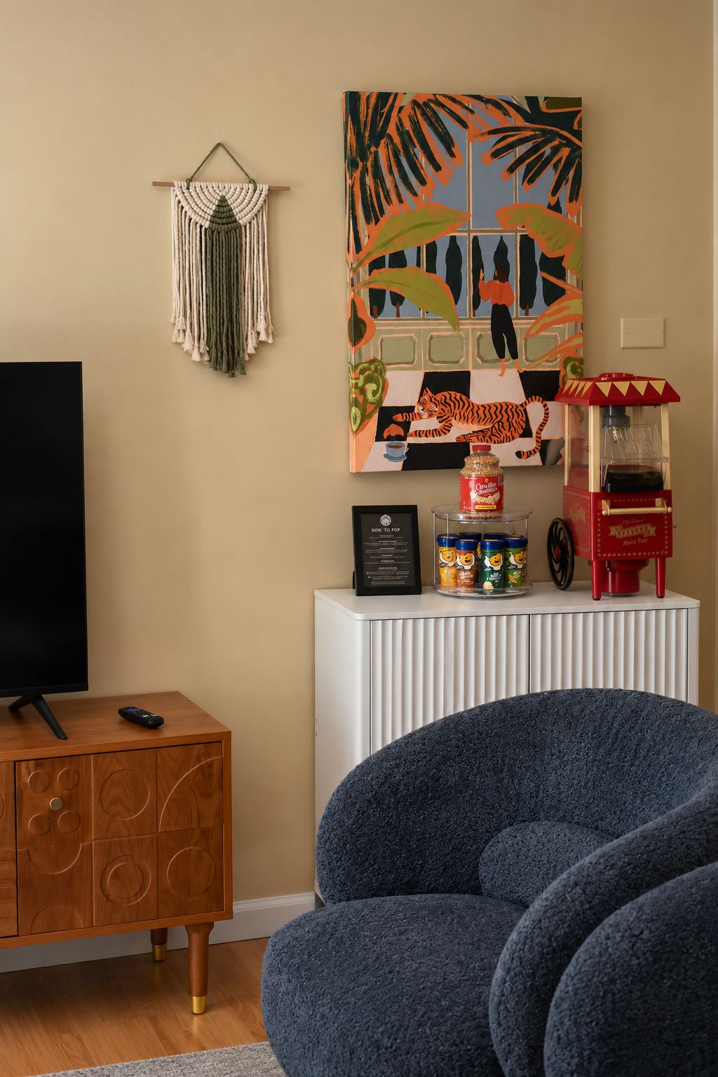 Olohuone, jossa on televisio, makramee-seinävaate, värikäs maalaus, popcorn-kone ja sininen sohva.
