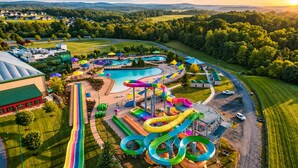 Eine Vogelperspektive eines Wasserparks mit mehreren Rutschen und Pools, umgeben von grünen Feldern und Wohngebieten.
