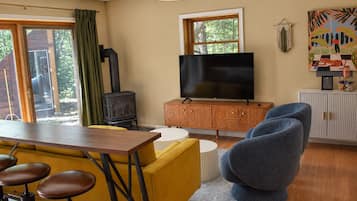 A cozy living room with a television, a wooden cabinet, a blue armchair, and a yellow sofa.