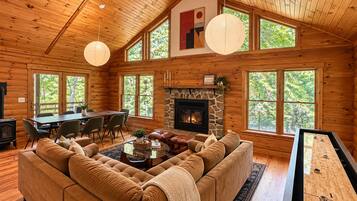 A cozy cabin interior with a stone fireplace, a sofa, a dining table, and a shuffleboard table.