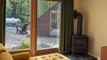 A modern living room with a yellow sofa, a fireplace, and a view of a wooden cabin through large sliding glass doors.