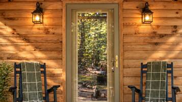 A wooden cabin with a door, two rocking chairs, and two wall-mounted lanterns.