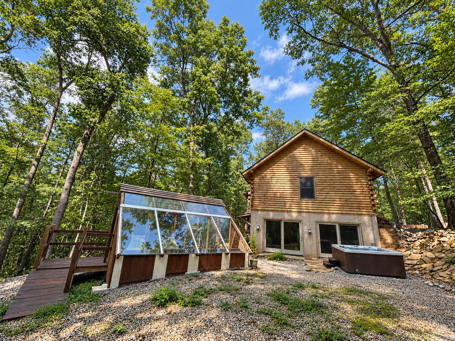 A log cabin with a glass-enclosed deck, surrounded by a forest.