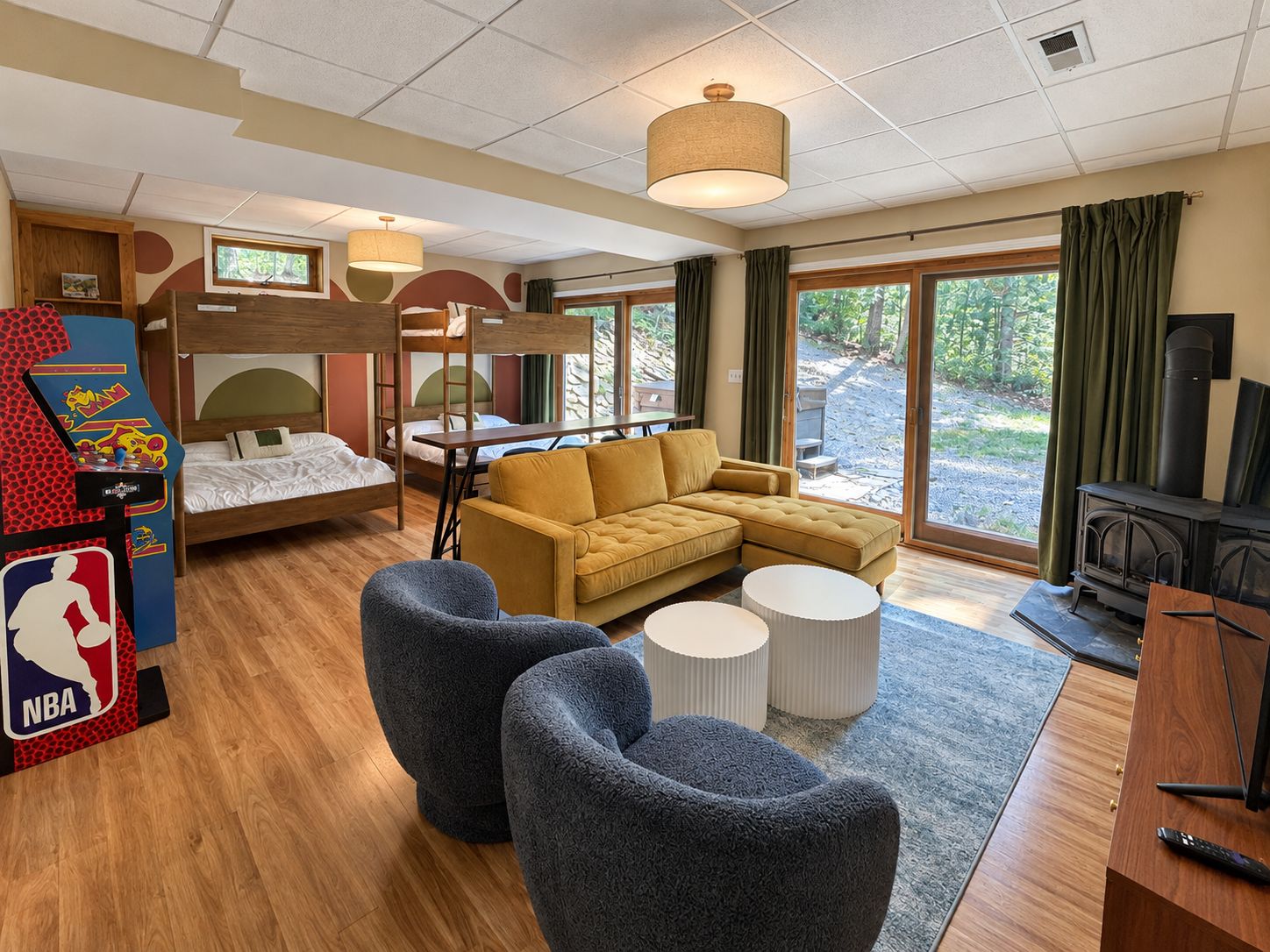 A hotel room with a bunk bed, a sofa, two ottomans, a small table, a fireplace, and a large window with curtains.
