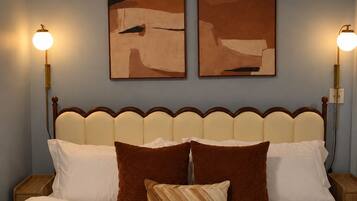 Una cama con sábanas blancas y almohadas marrones, flanqueada por dos cuadros colgados en la pared.
