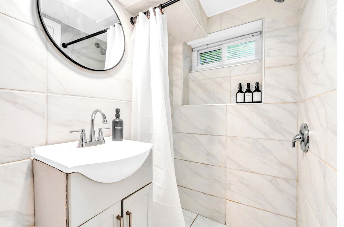 A bathroom with a white sink, a mirror, a shower curtain, and a shelf with toiletries.