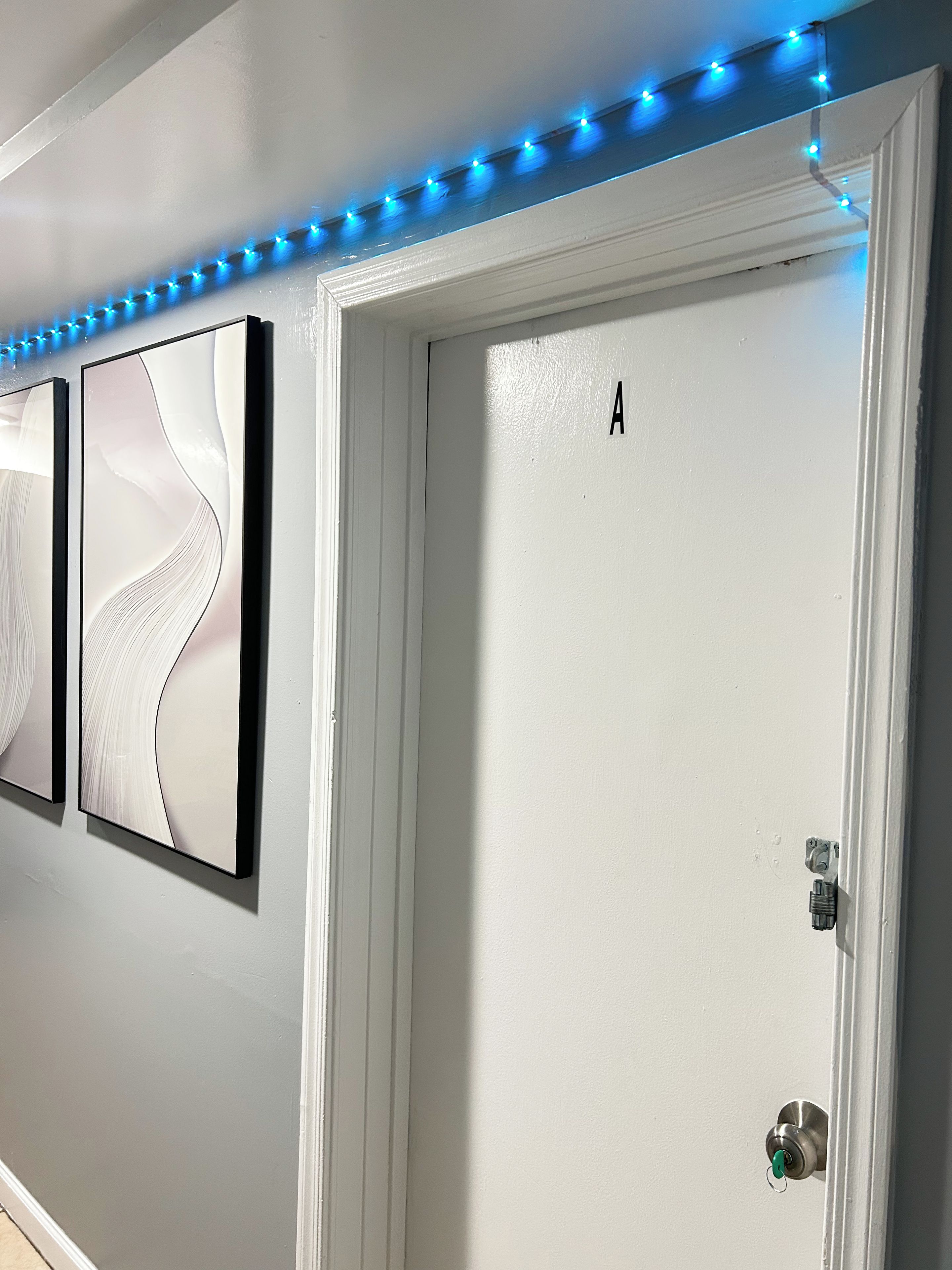 A hallway with a white door marked with the letter 'A', a wall-mounted light fixture, and a door handle.