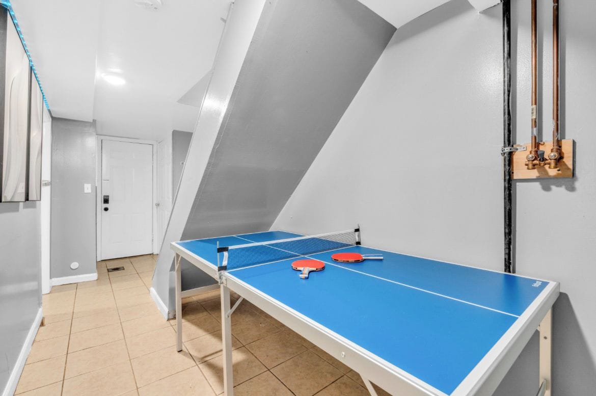 A ping pong table with two paddles and a table tennis ball in a room with a sloped ceiling and a door in the background.