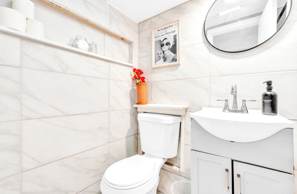 A bathroom with a toilet, a sink, a mirror, and a shelf with toiletries.