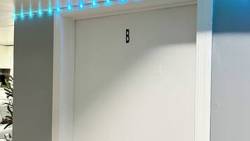 Een witte deur met een 'B'-aanduiding, een metalen deurklink en een rij blauwe lichtjes erboven.