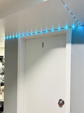 A white door with a 'B' marking, a metal door handle, and a string of blue lights above it.