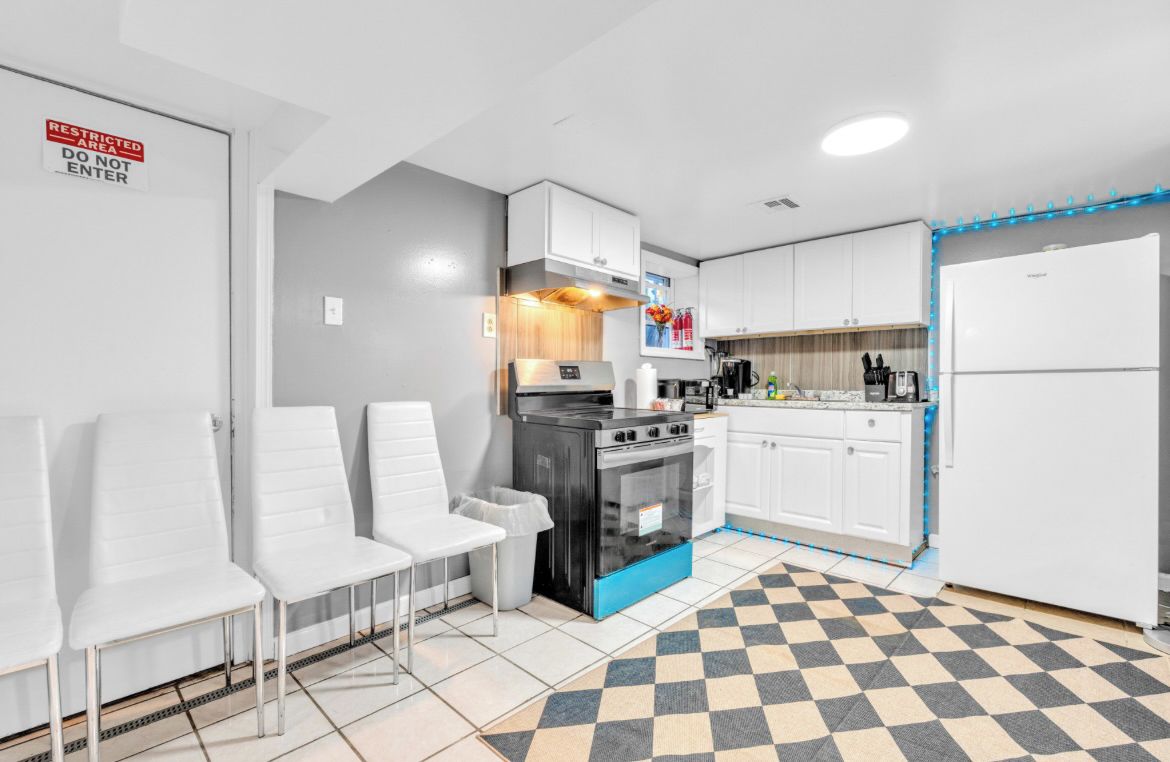 A modern kitchen with white cabinets, a black stove, and a white refrigerator. There is a checkered floor mat and a sign indicating a restricted area.