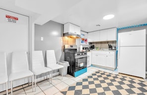 A modern kitchen with white cabinets, a black stove, and a white refrigerator. There is a checkered floor mat and a sign indicating a restricted area.