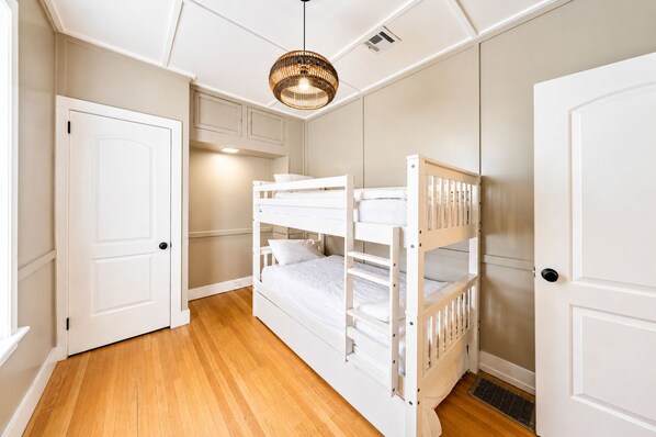 A room with bunk beds, a door, a ceiling light fixture, and a vent.
