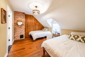 Une chambre avec un plafond en pente, un plancher en bois, un mur en briques et un lit recouvert de linge de lit blanc.