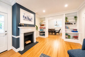 A living room with a fireplace, a dining area, and built-in shelving with books and decorative items.
