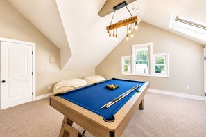 Une pièce avec une table de billard, un luminaire au plafond et une fenêtre donnant sur un paysage verdoyant.