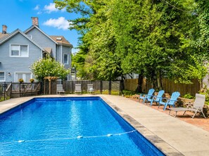 Une piscine rectangulaire à l’eau d’un bleu limpide, entourée d’une terrasse en bois et d’un mur en briques.