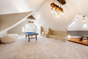 A spacious attic room with a pool table, a bean bag, a sofa, and a hanging light fixture.
