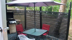 Une terrasse extérieure avec une table et des chaises, un barbecue et une clôture en bois.