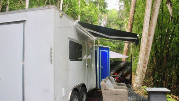 Un camping-car blanc avec une porte bleue et une véranda couverte.