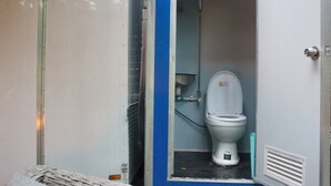 Des toilettes portables dotées d’un couvercle, d’un espace douche et d’un cadre de porte en métal.