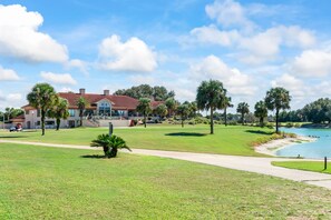 A golf course with a clubhouse, palm trees, and a body of water. - Townhome with Shared Pool, Wifi & Full Kitchen (Navarre)
