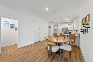 A modern kitchen with white cabinets, a stainless steel refrigerator, and a dining area with a round wooden table and wicker chairs. - Townhome with Shared Pool, Wifi & Full Kitchen (Navarre)