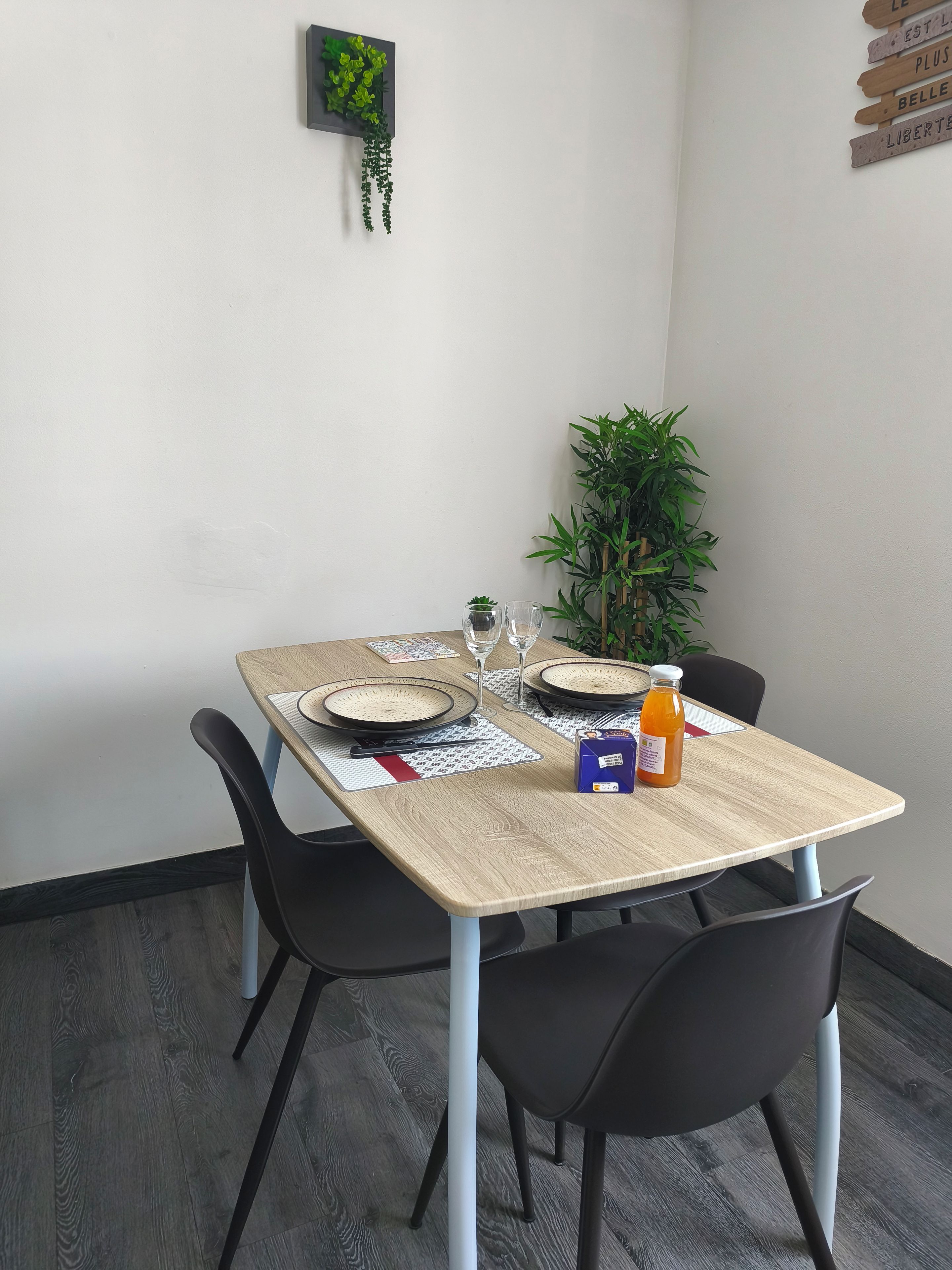 Une table à manger dressée avec des assiettes, des verres et une bouteille, entourée de chaises.