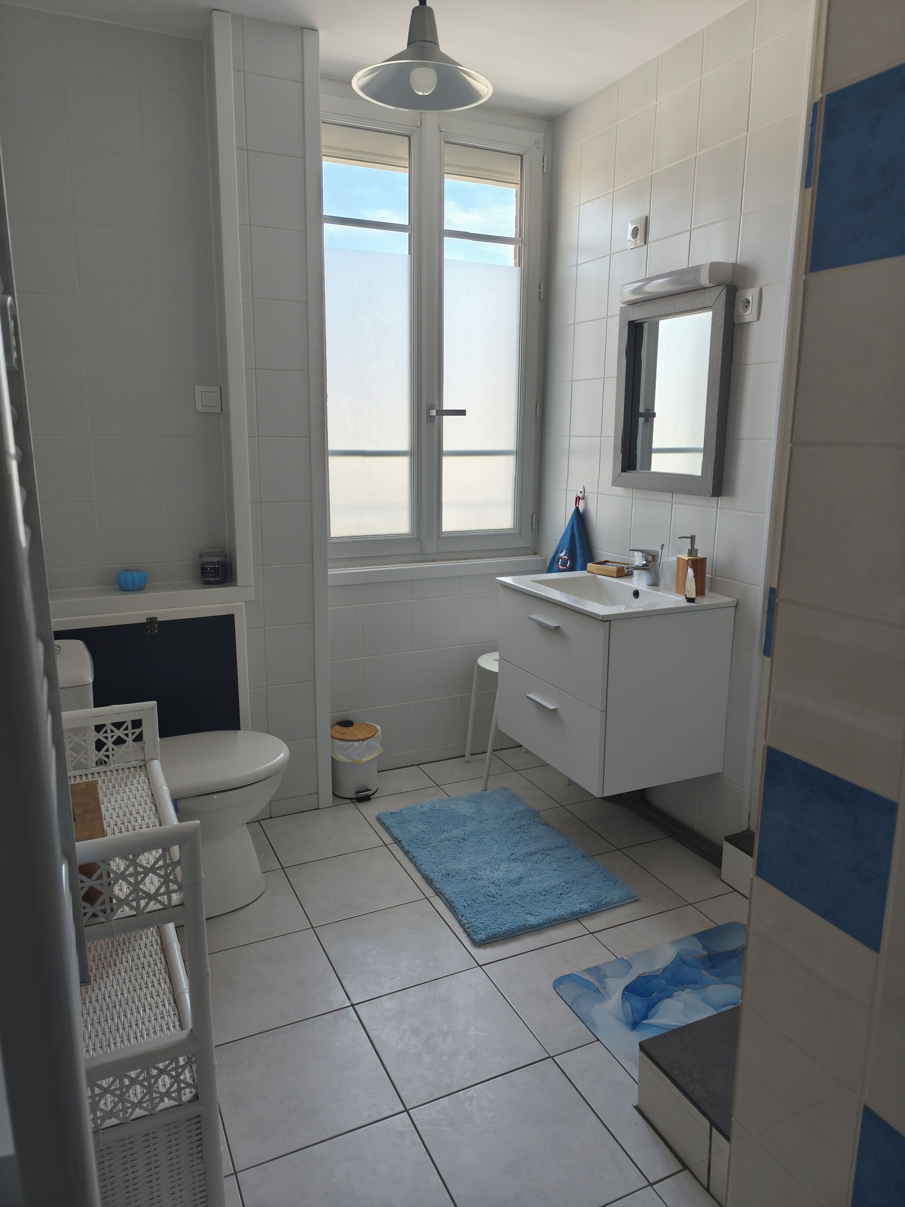 A bathroom with a toilet, sink, mirror, and window.