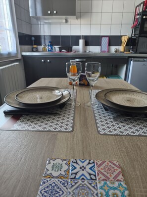 A dining table set with plates, glasses, and a bottle of orange juice. - Point Baie Studio 1 – Appartement confortable au cœur d’Abbeville (Abbeville)