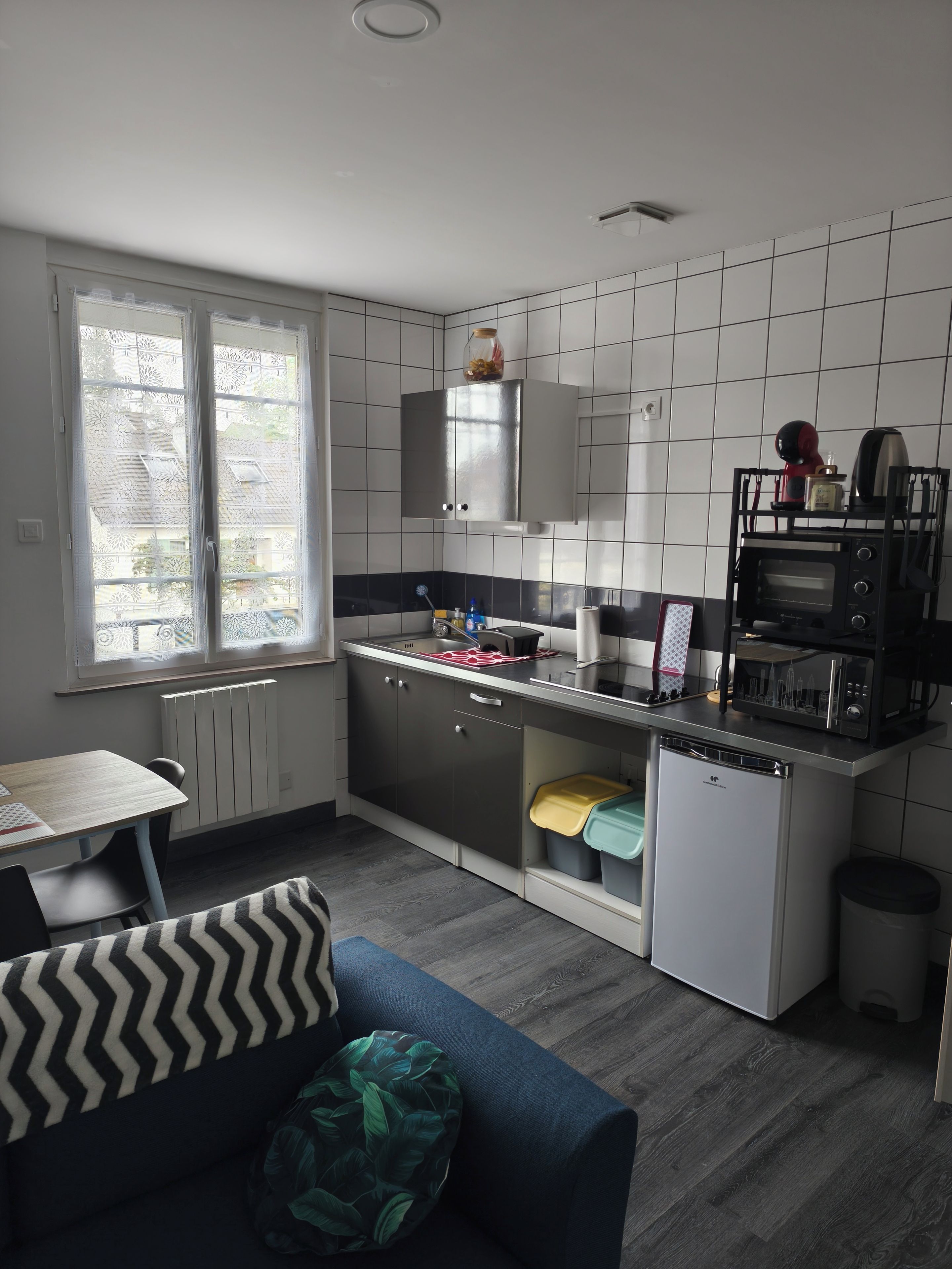 A compact kitchen with a dining area, a built-in oven, and a window with patterned curtains.