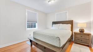 A bedroom with a bed, nightstand, lamp, and two windows with blinds. - Port Orford Coastal Retreat, Pet Friendly & Fire Pit (Port Orford)