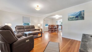 A spacious living room with a leather sofa, a dining table with chairs, and a kitchen area in the background. - Port Orford Coastal Retreat, Pet Friendly & Fire Pit (Port Orford)