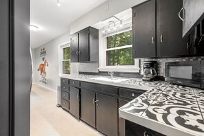 A modern kitchen with black cabinets, a patterned backsplash, and a window overlooking greenery. - Spacious 4-bedroom house in beautiful Hot Springs near Oaklawn (Hot Springs)