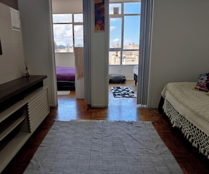 A room with a bed, a window, a door leading outside, and a view of the cityscape. - Bright 2BR Apt with Garage Near Ipanema & Copacabana (Rio de Janeiro)