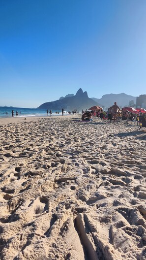 A beach with footprints leading to the water, a distant mountain, and beach umbrellas. - Bright 2BR Apt with Garage Near Ipanema & Copacabana (Rio de Janeiro)