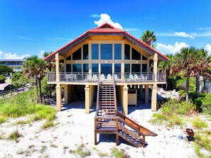 A beachfront building with a balcony, a staircase leading to the entrance, and a sandy foreground. - Island Dream  Beachfront Plantation Home  2 Kings + Bunk Room  Sleeps 10 (Eastpoint)