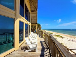 Une terrasse en bois avec des chaises blanches donnant sur une plage.