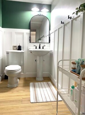 Ein Badezimmer mit Toilette, Waschbecken, Spiegel und einem Ablagefach für Pflegeprodukte.