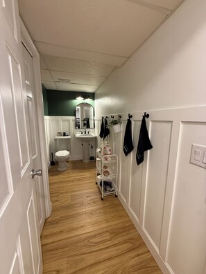 Ein Flur mit einer weißen Tür, einem weißen Waschbecken, einer Toilette und einem Spiegel.