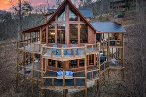 A multi-level wooden cabin with a balcony and outdoor seating area. - Stunning Mountain Views - Hot Tub + EV Charger! (Mineral Bluff)